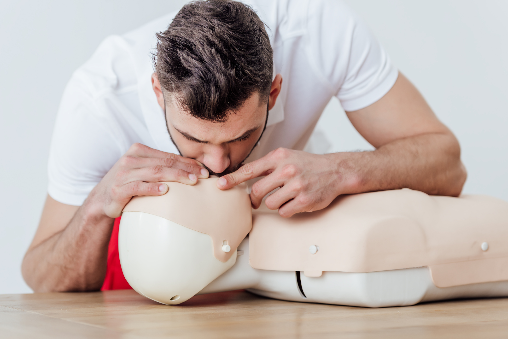 man using mouth to mouth technique on dummy during cpr training isolated on grey